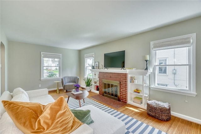living room featuring baseboards, a brick fireplace, arched walkways, and wood finished floors