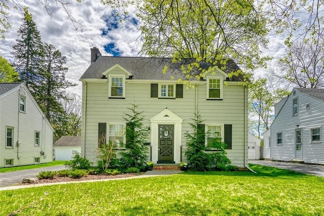 colonial house with a garage, a front lawn, and a chimney