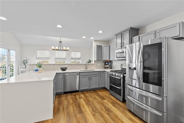 kitchen featuring a sink, light wood-style floors, stainless steel appliances, a peninsula, and gray cabinetry