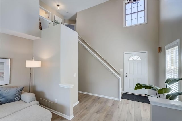 entryway featuring baseboards, light wood finished floors, and a towering ceiling