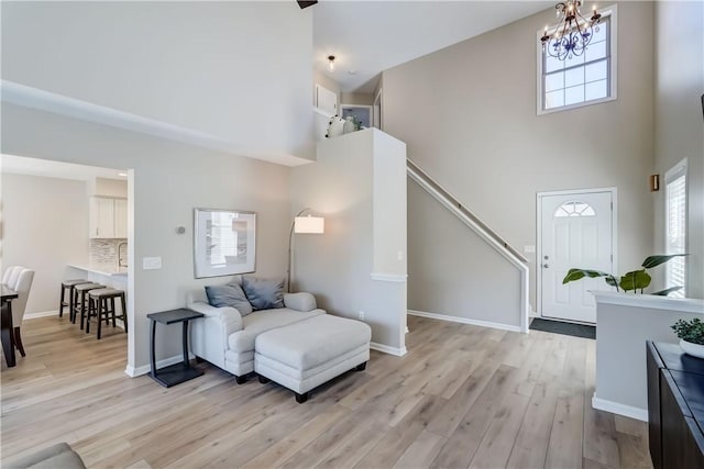 living room featuring a high ceiling, a chandelier, baseboards, and light wood finished floors