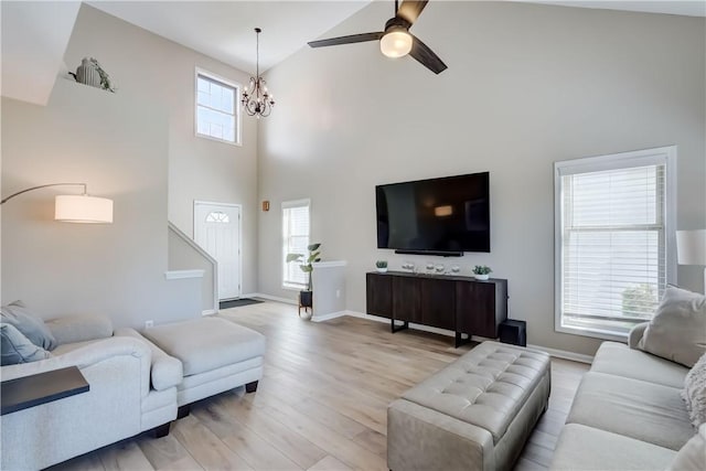 living room featuring light wood-style floors, high vaulted ceiling, baseboards, and ceiling fan with notable chandelier