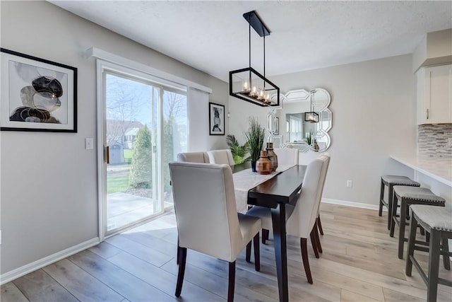 dining area featuring baseboards, an inviting chandelier, and light wood-style flooring