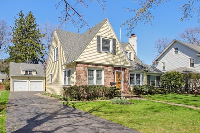 new england style home featuring driveway, a chimney, a front yard, an outdoor structure, and stone siding