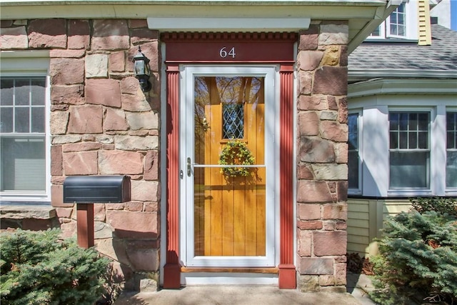entrance to property featuring roof with shingles and stone siding
