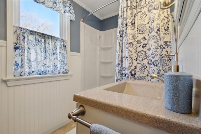 bathroom featuring wainscoting, walk in shower, ornamental molding, and a sink