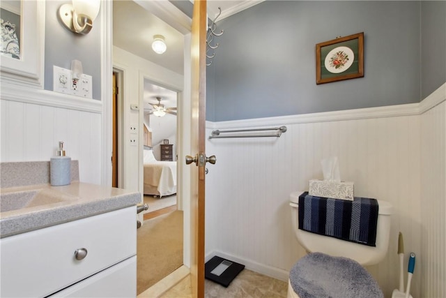 ensuite bathroom featuring vanity, ceiling fan, ensuite bath, and a wainscoted wall