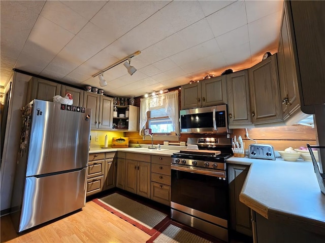 kitchen featuring appliances with stainless steel finishes, track lighting, a sink, light wood-style floors, and light countertops