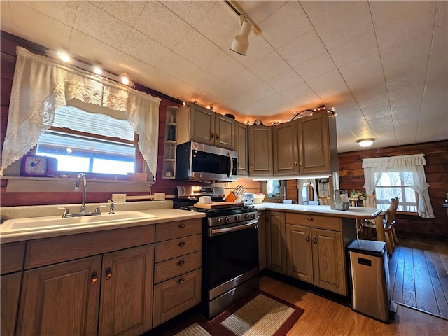 kitchen with a peninsula, light wood-type flooring, light countertops, a sink, and appliances with stainless steel finishes