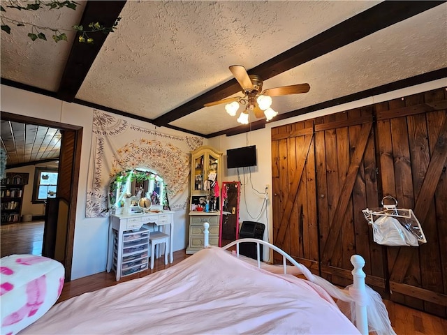 bedroom with a textured ceiling, ceiling fan, beam ceiling, and wood finished floors