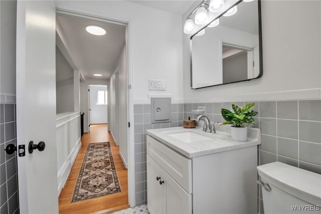 bathroom with tile walls, a wainscoted wall, vanity, and toilet