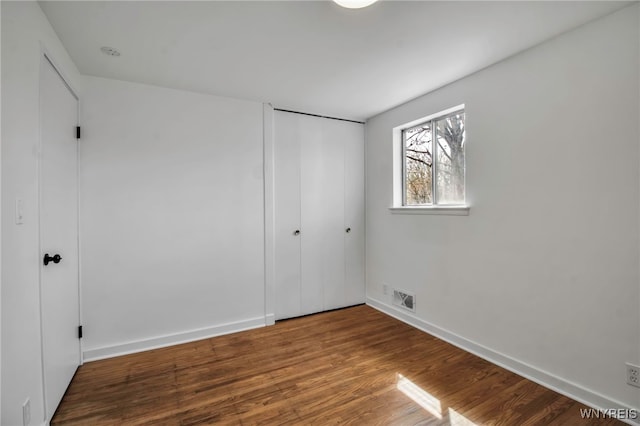unfurnished bedroom with baseboards, wood finished floors, visible vents, and a closet