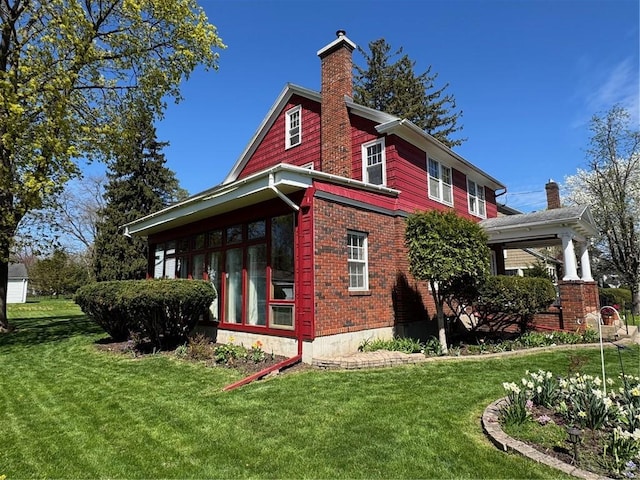 view of property exterior featuring a lawn, brick siding, a chimney, and a sunroom
