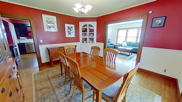 dining space featuring crown molding, wainscoting, wood finished floors, baseboards, and a notable chandelier