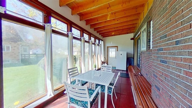 sunroom / solarium featuring beamed ceiling, outdoor dining area, and brick wall