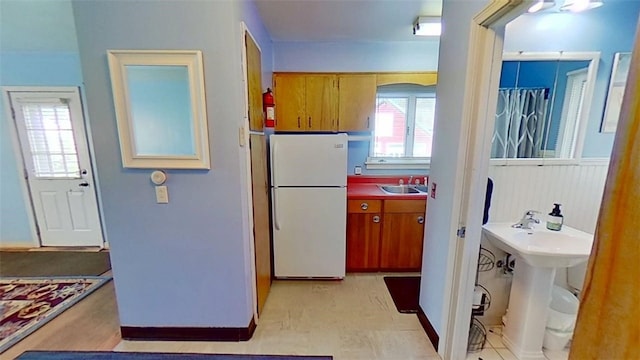 kitchen featuring brown cabinets, a sink, arched walkways, freestanding refrigerator, and baseboards