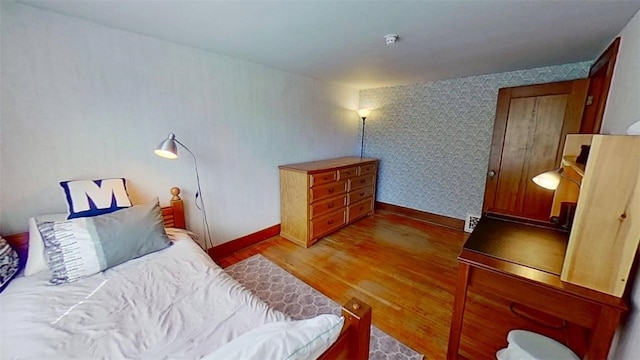 bedroom featuring baseboards, wallpapered walls, and wood finished floors