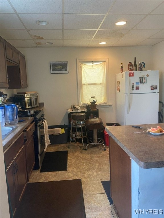 kitchen featuring freestanding refrigerator, dark brown cabinetry, a paneled ceiling, and stainless steel range with electric cooktop