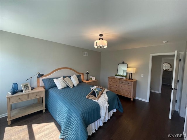 bedroom with baseboards, visible vents, and wood finished floors