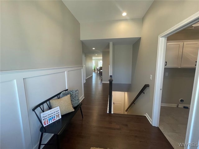 corridor with a wainscoted wall, dark wood-style flooring, and an upstairs landing