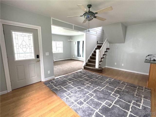 foyer with stairs, wood finished floors, baseboards, ceiling fan, and a baseboard heating unit