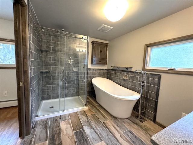 bathroom with visible vents, wood finished floors, tile walls, a freestanding bath, and a stall shower