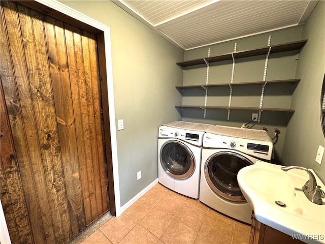 clothes washing area with baseboards, a sink, light tile patterned flooring, and washing machine and clothes dryer