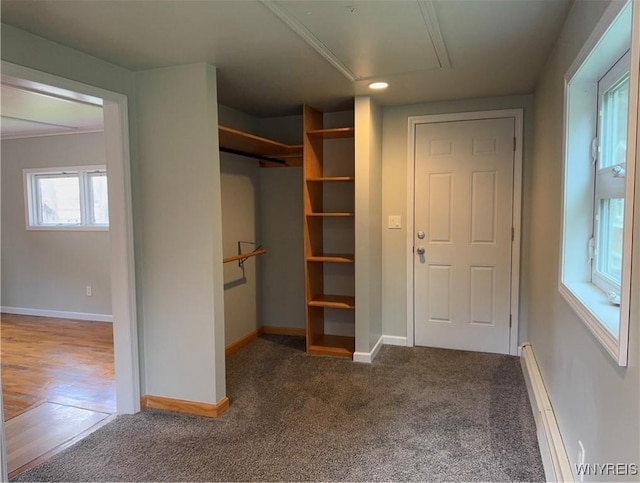 unfurnished bedroom with carpet flooring, attic access, baseboards, a baseboard radiator, and a closet