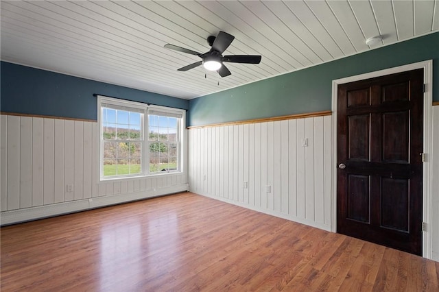 empty room featuring wooden walls, a ceiling fan, wood finished floors, a baseboard heating unit, and wood ceiling