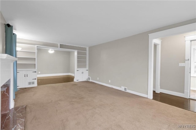 unfurnished living room featuring baseboards, visible vents, carpet, and a premium fireplace