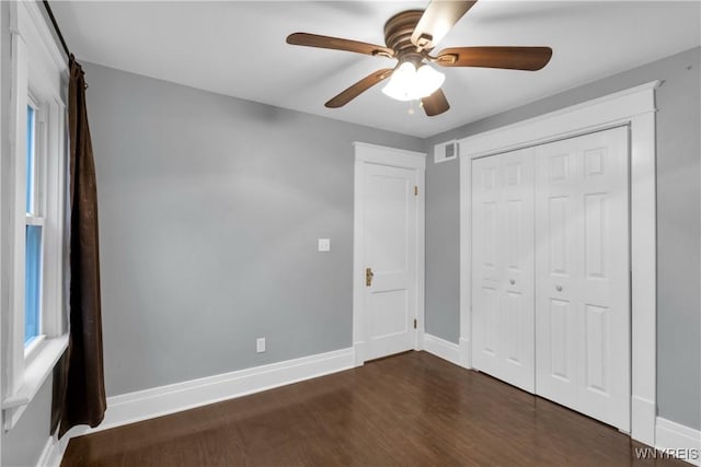 unfurnished bedroom with ceiling fan, baseboards, dark wood-type flooring, visible vents, and a closet