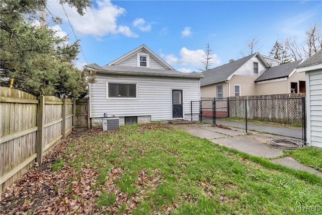 rear view of property featuring a lawn, a fenced backyard, central AC, and a gate
