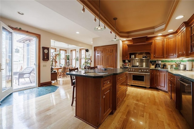kitchen with high end stainless steel range, a sink, dishwasher, light wood-type flooring, and a kitchen bar