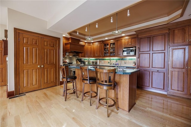 kitchen with custom exhaust hood, a kitchen island, dark countertops, a raised ceiling, and stainless steel microwave