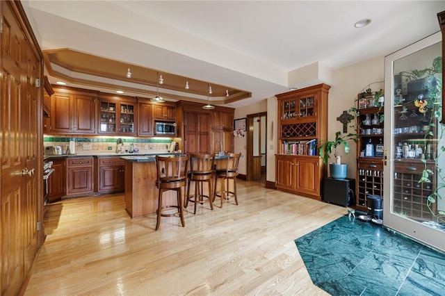 bar with light wood-type flooring, recessed lighting, a raised ceiling, stainless steel microwave, and tasteful backsplash