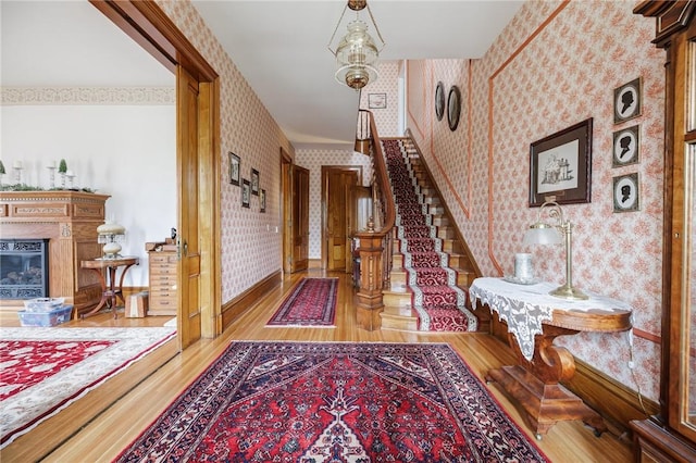 hall featuring stairway, baseboards, wallpapered walls, and wood finished floors