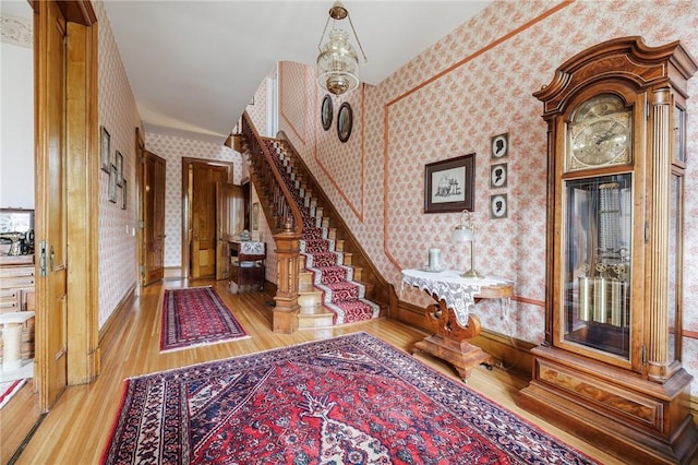 foyer entrance with wallpapered walls, baseboards, stairway, and light wood-type flooring