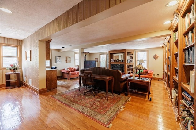 living room with light wood finished floors, a textured ceiling, baseboards, wallpapered walls, and visible vents