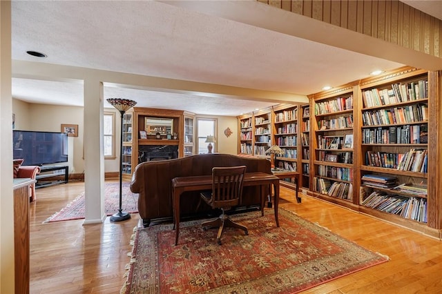 sitting room featuring a textured ceiling, baseboards, bookshelves, and wood finished floors