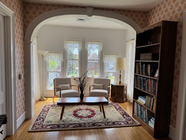 sitting room featuring arched walkways, wallpapered walls, visible vents, and wood finished floors