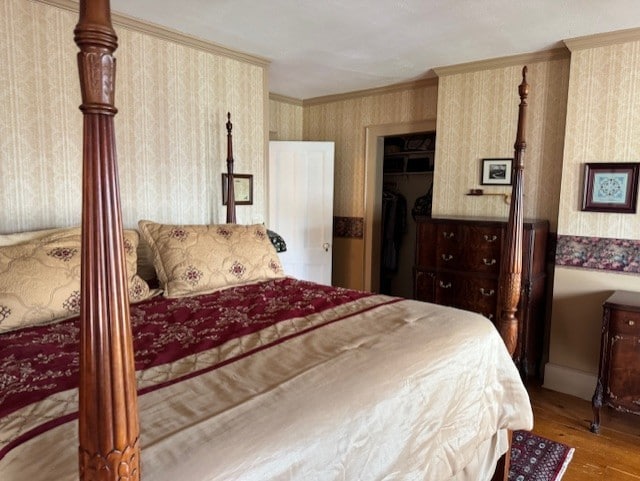 bedroom with ornamental molding, wood finished floors, and wallpapered walls