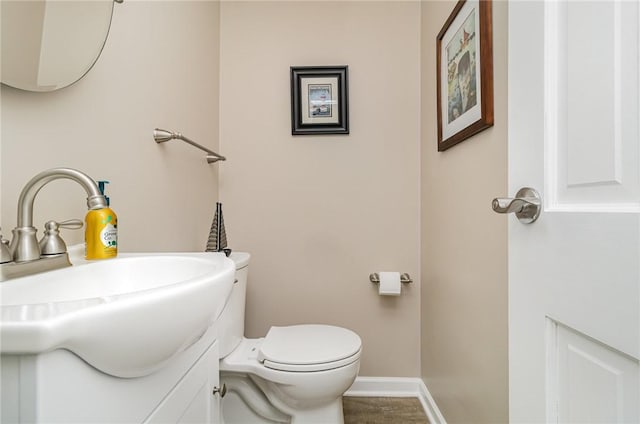 half bathroom with baseboards, vanity, and toilet