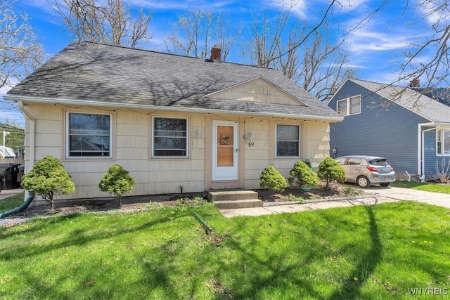 view of front of home with roof with shingles, a front yard, and a chimney