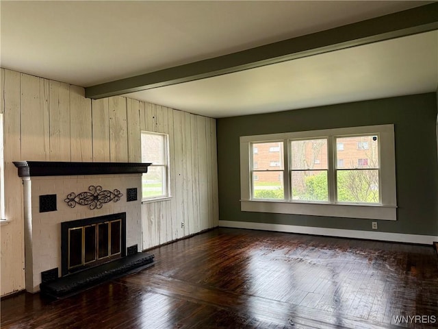 unfurnished living room featuring a fireplace, wood walls, beam ceiling, baseboards, and dark wood-style floors