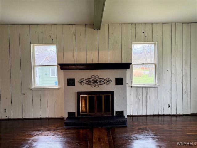 unfurnished living room with plenty of natural light, a fireplace, wood walls, and wood finished floors