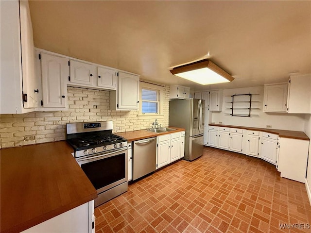 kitchen featuring appliances with stainless steel finishes, tasteful backsplash, a sink, white cabinets, and brick patterned floor