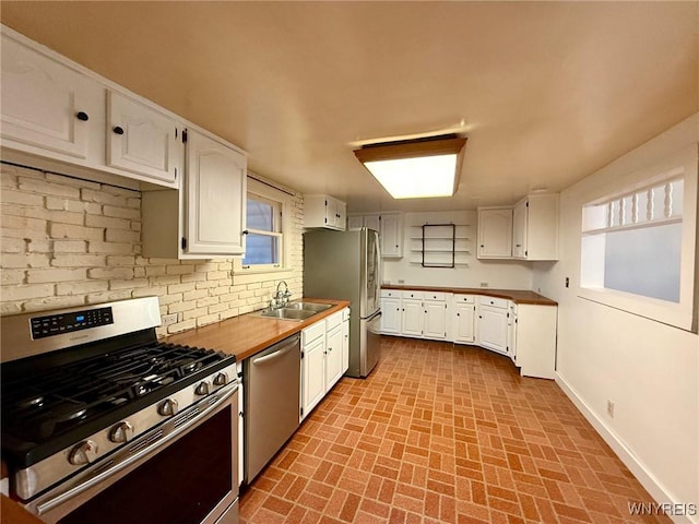 kitchen with appliances with stainless steel finishes, white cabinets, and brick patterned floor