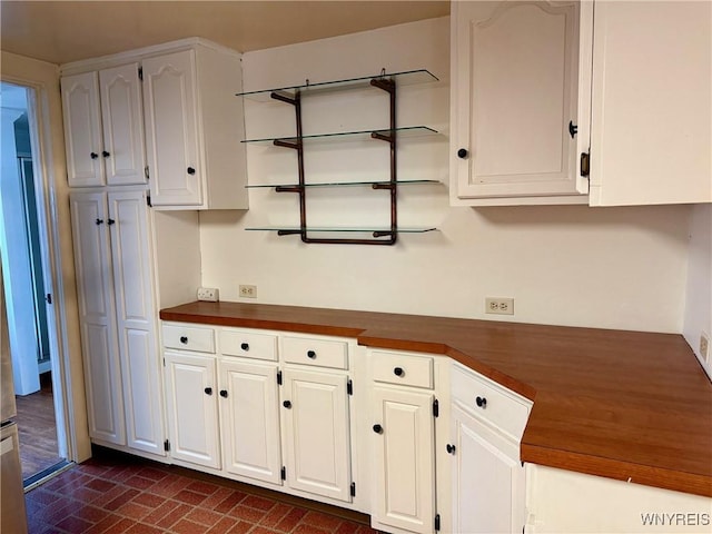 kitchen featuring open shelves, brick patterned floor, and white cabinetry