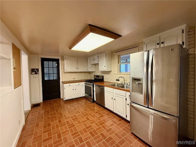 kitchen featuring white cabinets, appliances with stainless steel finishes, brick patterned floor, and a sink