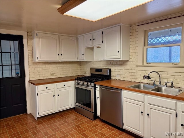 kitchen featuring a sink, white cabinets, brick patterned floor, and stainless steel appliances